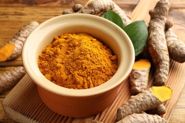 Turmeric powder in bowl, roots and leaves on table, closeup