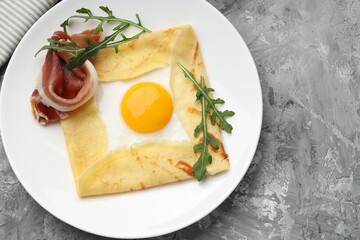 Delicious crepe bretonne with bacon and arugula on grey textured table, top view