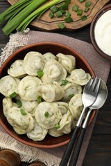Tasty dumplings with green onion and dill in bowl served on wooden table, flat lay