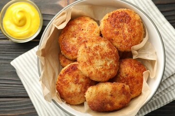 Tasty patties in bowl and mustard on wooden table, flat lay