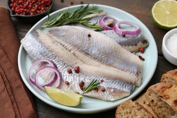 Marinated herring fillets with onion rings, rosemary, lime and spices on wooden table, closeup