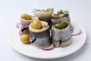 Delicious herring rolls with olives, pickles, dill and onion on light table, closeup