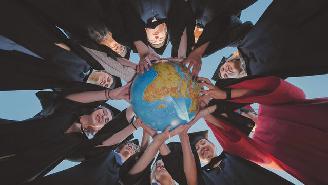 Smiling graduates in academic gowns holding a globe, representing readiness to embrace global opportunities and create positive change