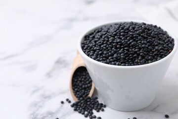 Black lentils on white marble table, closeup. Space for text