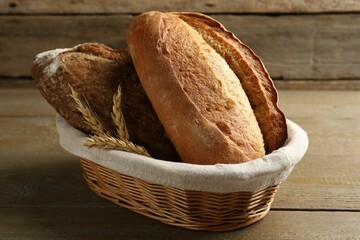 Different loaves of fresh bread and spikes in wicker basket on wooden table, closeup