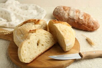 Slices of fresh bread and knife on light textured table, closeup
