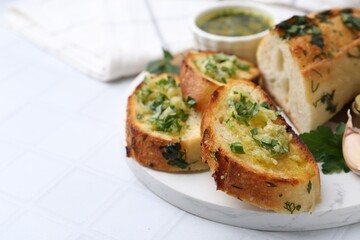 Tasty bread with garlic, herbs and oil on white tiled table, closeup. Space for text