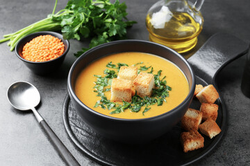 Delicious lentil cream soup served with croutons on grey table, closeup