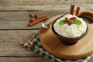 Delicious rice pudding with almonds, mint and cinnamon sticks served on wooden table, closeup