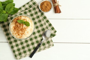 Delicious rice pudding with cinnamon, mint and spoon on white wooden table, flat lay. Space for text