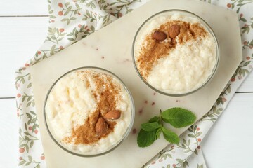 Delicious rice pudding with cinnamon, almonds and mint on white wooden table, top view