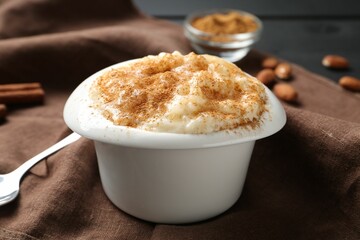 Delicious rice pudding with cinnamon in bowl, almonds and spoon on table, closeup