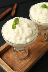 Delicious rice pudding with mint in glass dessert bowls on black table, closeup