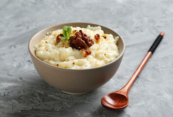 Delicious rice pudding with walnuts, mint and spoon on grey table, closeup
