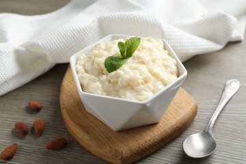 Delicious rice pudding with almonds, mint and spoon on wooden table, closeup