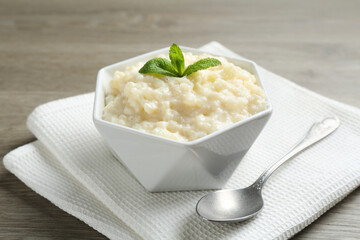 Delicious rice pudding in bowl, mint and spoon on wooden table, closeup