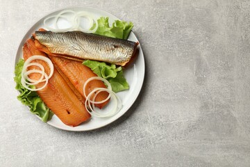 Delicious smoked herring fillets with onions and lettuce on grey table, top view. Space for text