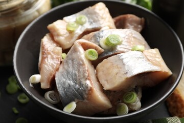 Pieces of delicious herring with green onions on black table, closeup