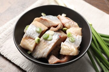 Pieces of delicious herring with green onions on wooden table, closeup
