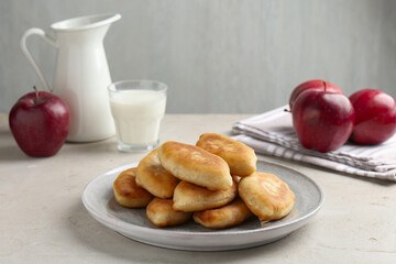 Delicious fried pyrizhky (stuffed pies), apples and milk on light grey table, closeup