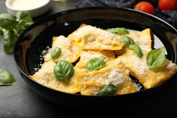Delicious ravioli with parmesan cheese and basil on black table, closeup