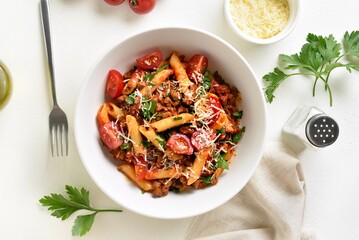 Bowl of bolognese penne pasta with minced meat, tomatoes and greens