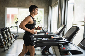 Fototapeta premium Young man jogging on treadmill at modern gym with natural light, focused on fitness goal, exercising to maintain health and improve endurance