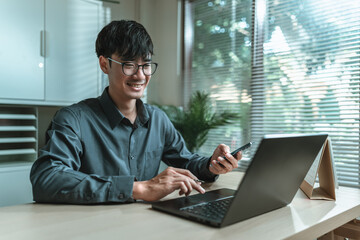 Smile Businessman uses mobile phone to check news, email, market information, stocks while working with laptop in Office.