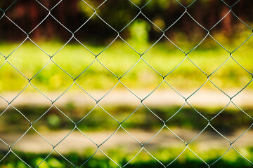 Metal mesh fence separating green grass from the rest of the world