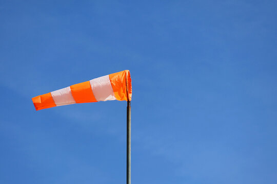 Orange and white striped wind sock against a blue sky. A conically shaped tube of woven textile used to indicate wind direction and speed. Aircraft wind indicator.