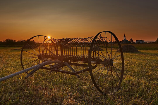 Antique hay tedder in a meadow at sunset