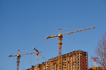 Two cranes near a multi-storey building under construction against a blue sky