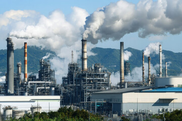 Obraz premium Industrial pollution scene with an oil refinery emitting smoke over a mountainous landscape