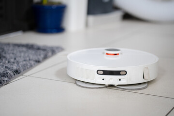 White robot vacuum cleaner on the  floor in bedroom. Cleaning the apartment with a modern smart vacuum cleaner