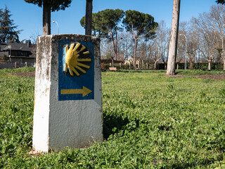 Stone monolith, quite deteriorated, located in a green grass park indicating the direction to follow for pilgrims of the Camino de Santiago on their long journey to reach Santiago de Compostela
