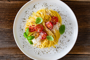 Spaghetti with cherry tomatoes, parmesan cheese, olive oil and basil leaves served on wooden table