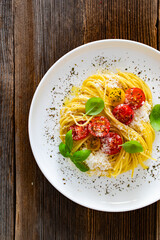 Spaghetti with cherry tomatoes, parmesan cheese, olive oil and basil leaves served on wooden table