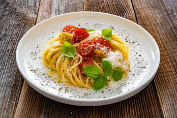 Spaghetti with cherry tomatoes, parmesan cheese, olive oil and basil leaves served on wooden table