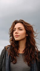 Fototapeta premium Young Woman with Wavy Hair Gazing Thoughtfully at Overcast Sky