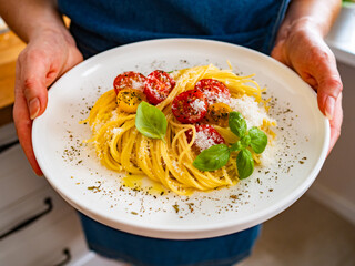 Woman holding plate with cherry tomatoes pasta with parmesan cheese, olive oil and basil leaves