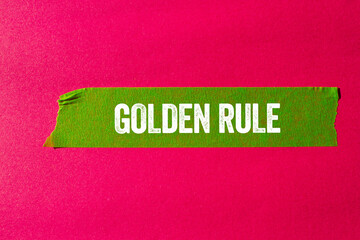 Golden rule message written on ripped torn green paper tape on pink background. Conceptual golden rule symbol. Copy space.