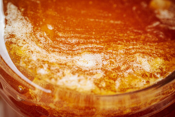  Close-up view of bubbly, fermenting honey in a glass jar on a rustic wooden surface. The frothy texture and amber color are prominent. 