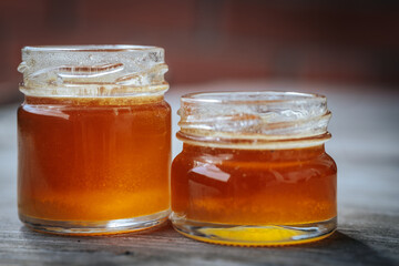 Close-up of two small glass jars filled with golden amber honey placed on a rustic wooden surface with a blurred background.