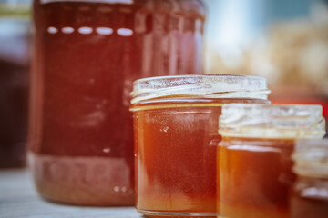 Close-up of two small glass jars filled with golden amber honey placed on a rustic wooden surface with a blurred background.