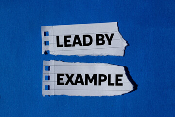 Lead by example message written on ripped torn white paper pieces on blue background. Conceptual...