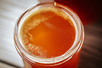 A close-up view of bubbling, fermenting honey in a glass jar on a rustic wooden surface. The bubbling texture and amber color are noticeable.