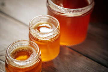 A series of small glass jars filled with golden honey arranged in a shallow depth of field on a rustic surface, creating a soft and warm composition with copy space.