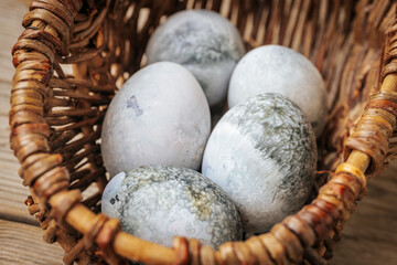 Close-up of several eggs with unique marble patterns in shades of gray, green and white, placed in a wicker basket. Earth tones and natural lighting.