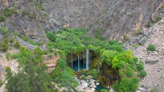 An impressive drone shot zooming in on Yer K&ouml;pr&uuml; Waterfall, a hidden paradise in the Mut district. The clear waters flowing between high cliffs form a natural pool surrounded by lush vegetation.