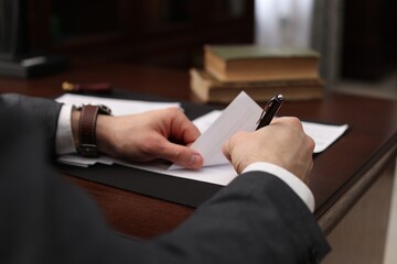 Notary signing document at wooden table in office, closeup